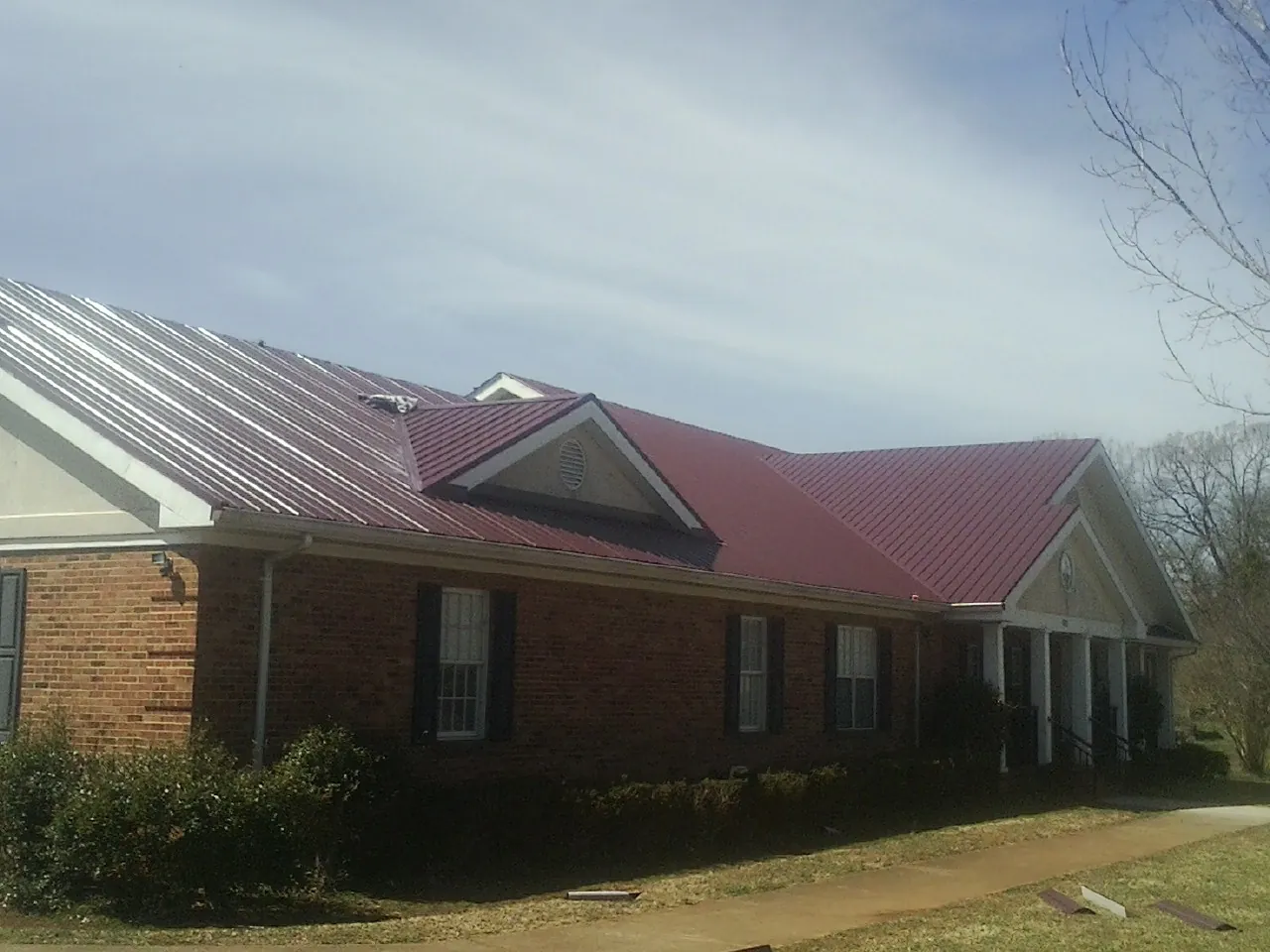 Red metal roof with gabled entries on a long brick building, from a Hail Damage Roof Repair job in Eden Prairie