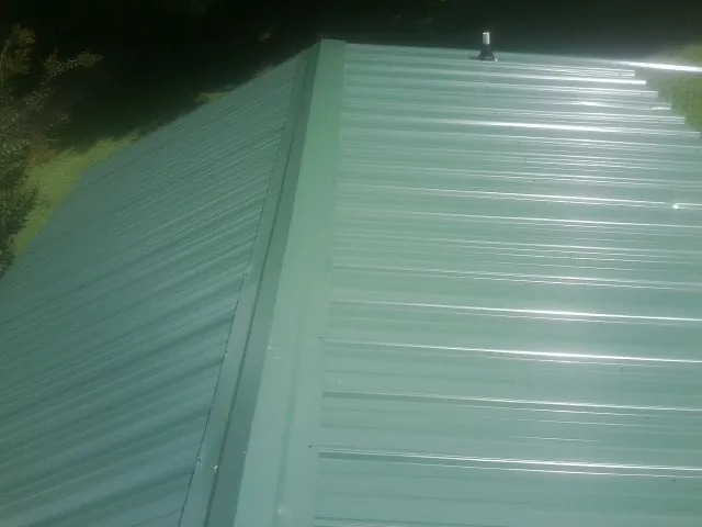 New green metal panels meeting at the ridge of a roof — Flat Roof Repair work by our crew in Eden Prairie