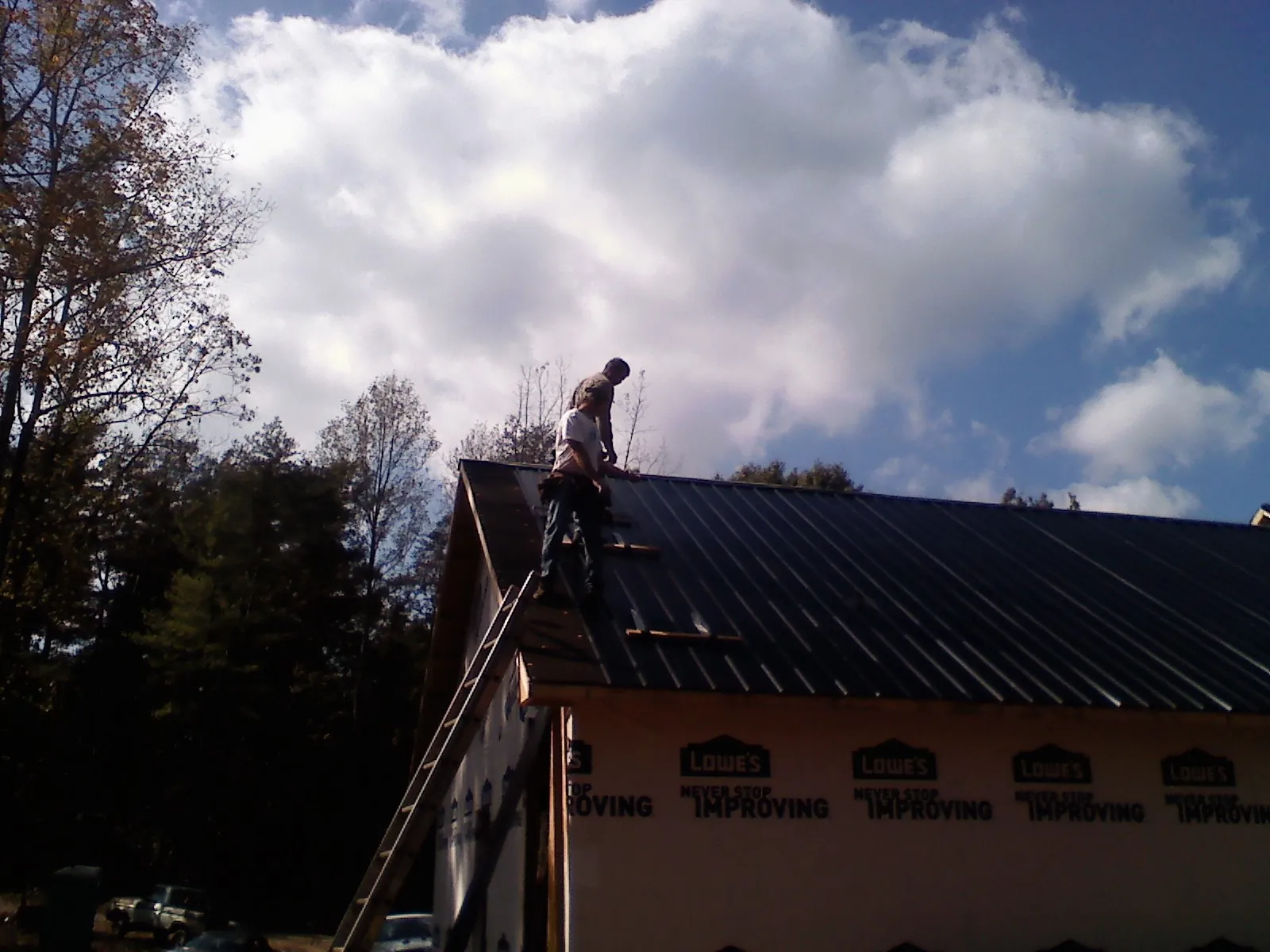 Roofer fastening dark metal panels high against a cloudy sky, from a Roof Inspection job in Eden Prairie