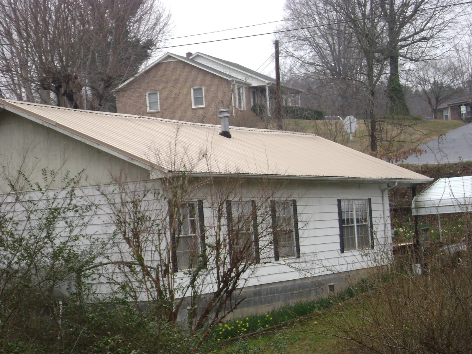 Tan metal roof on a white sided house set into a hillside — Commercial Roofing by Roofing Brothers in Eden Prairie